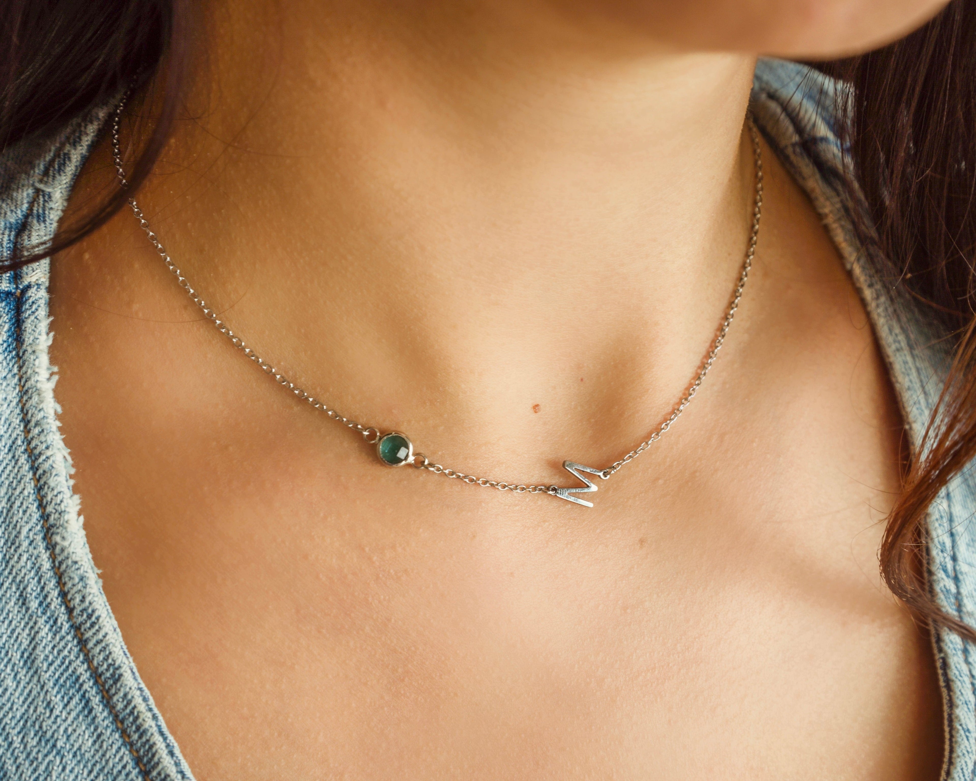Necklace with a small pendant on a person wearing a denim shirt.